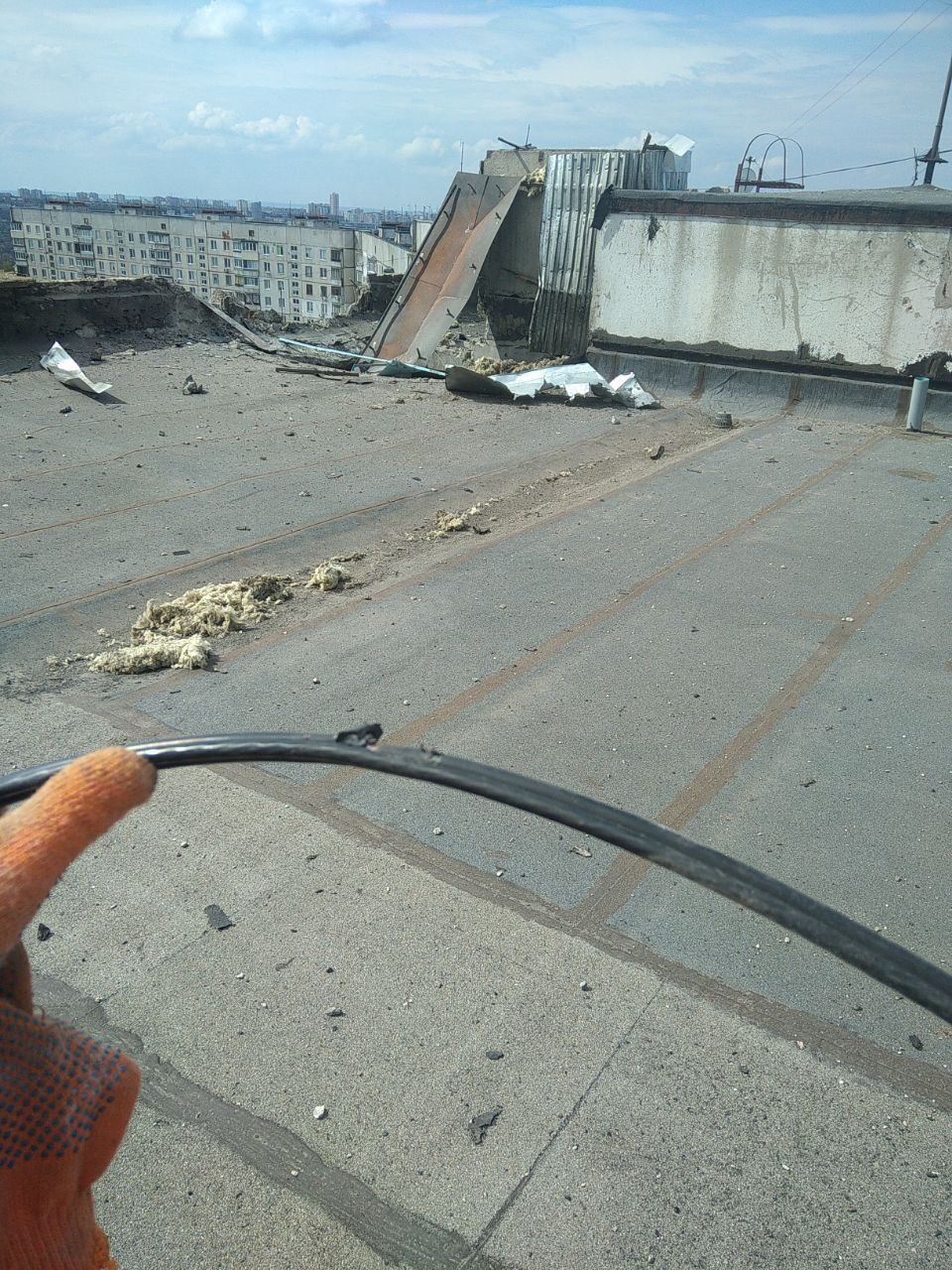 View from a rooftop of a gloved hand holding frayed fiber and showing some destruction on the roof